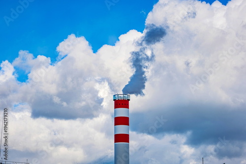 Картината върху платно Red and white striped industrial chimney emitting dark smoke into a cloudy blue