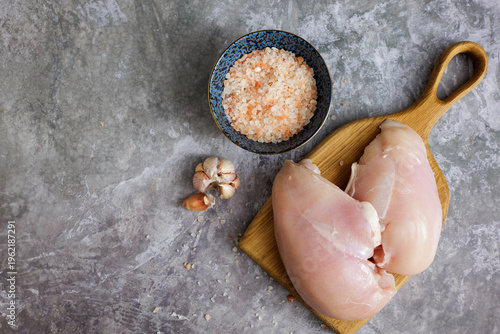 Uncooked chicken breasts prepared on a wooden cutting board with Himalayan salt and garlic cloves for a healthy meal
