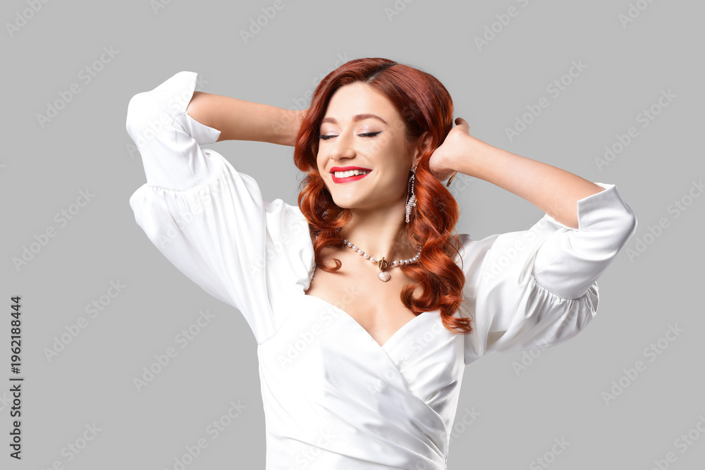 Naklejka premium Beautiful young lady with red wavy hair on grey background