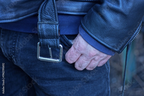 one hand of a man in a black leather jacket in the pocket of his gray jeans on an autumn day street