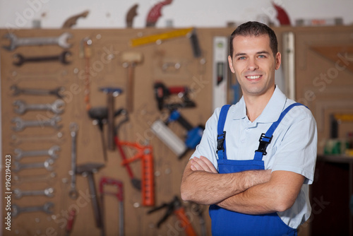 Fotografía Portrait of a confident male mechanic or handyman in blue overalls standing with arms crossed in a well-equipped workshop