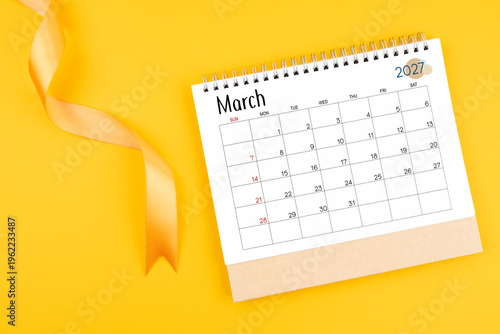 March 2027 desk calendar with yellow ribbon on yellow color background.