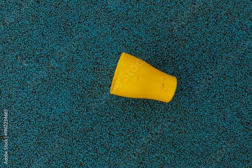 A yellow cup rests on a blue textured surface showing signs of wear and use
