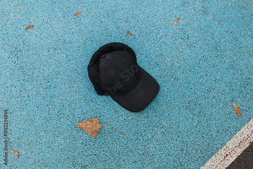 A black cap rests on a blue ground with some dry leaves scattered around it in a park area