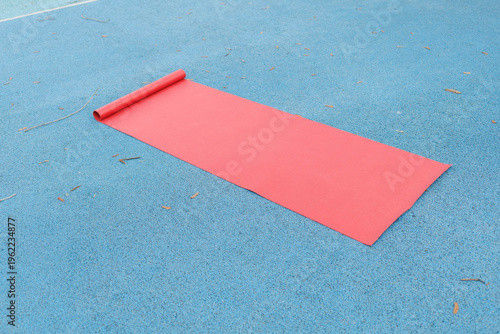 A red mat is unrolled on a blue surface in a sports area under clear sky