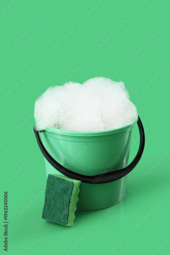 Fototapeta premium Plastic bucket with foam and sponge on green background