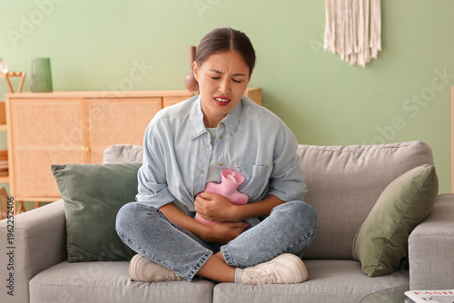Photography Young Asian woman with hot water bottle suffering from stomach ache on sofa in l
