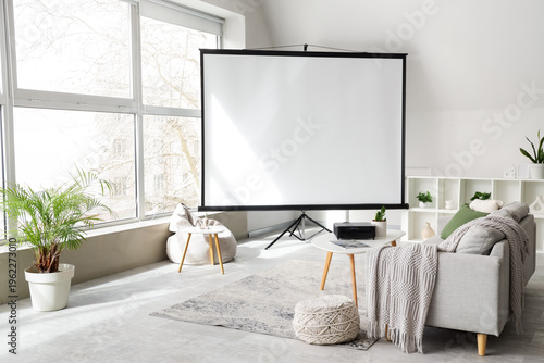 Interior of light living room with blank projector screen, sofa and table