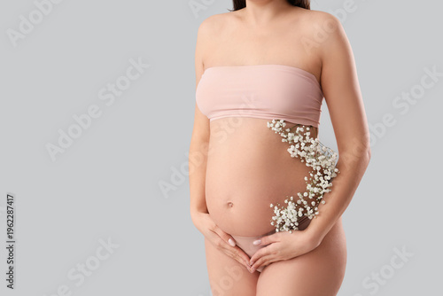 Young pregnant woman in underwear with flowers on light background
