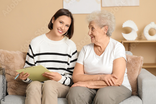 Smiling nurse with clipboard and senior woman sitting on sofa at home