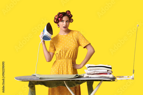Young woman ironing clothes on yellow background