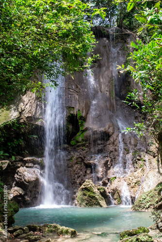 Scenic Alam Kandung Waterfall in East Java, Indonesia. Clear turquoise pool and flowing water framed by dense tropical forest and rocky cliffs.
