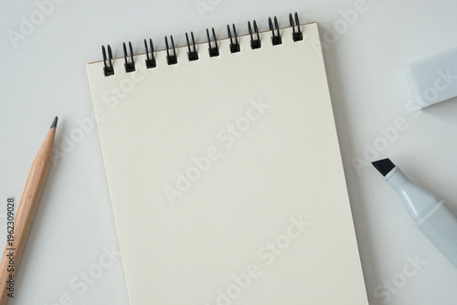 Blank spiral notebook with pencil and marker on white background, top-down view.