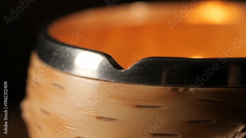 Close up of a burning candle in a birch bark holder with a metal rim, creating a warm and cozy atmosphere, perfect for relaxation and home decor