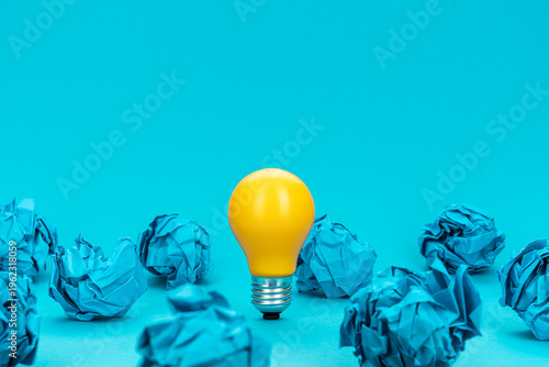 Great idea concept with bulb and crumpled office paper. Concept of inspiration, idea generation and problem solving. Conceptual photo of light bulb standing on turquoise blue background.