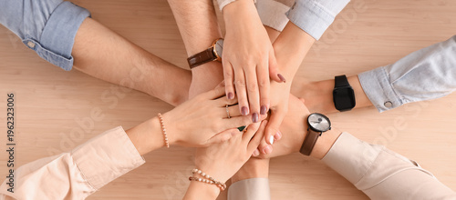 Group of people putting hands together on table, top view
