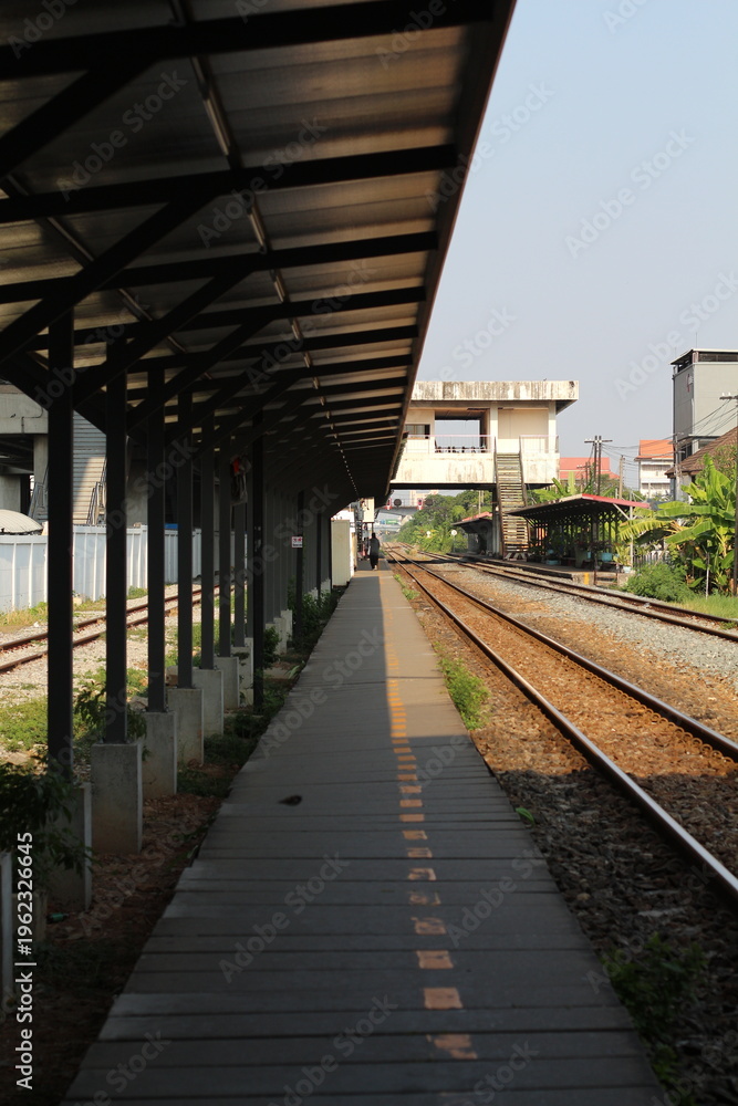 Fototapeta premium Empty train station platform with tracks stretching into the distance under a shelter