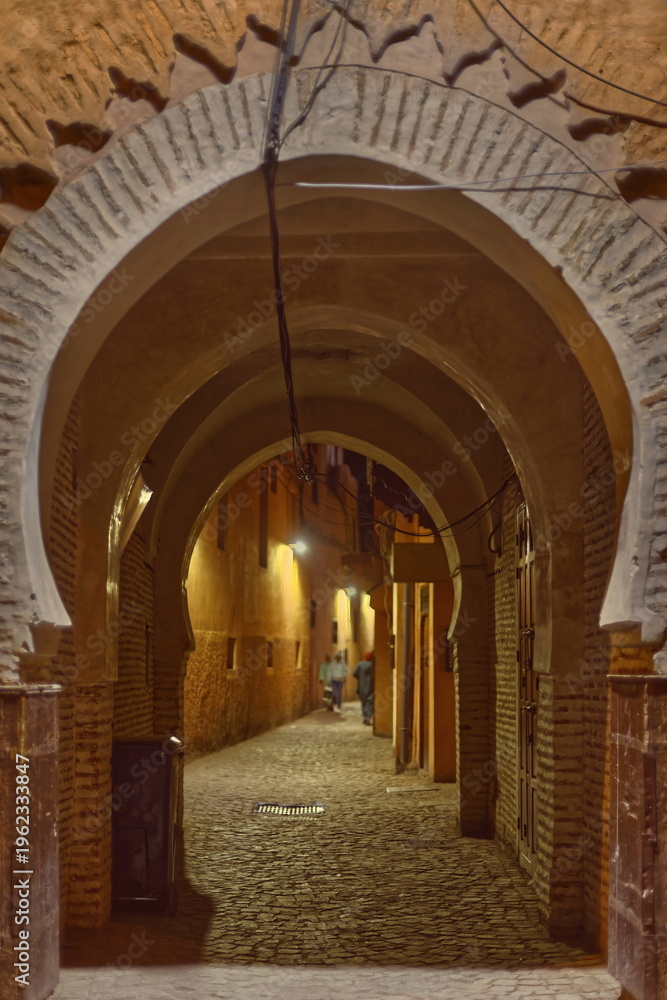 Obraz premium Night horseshoe-arched passage under traditional houses, lit by the street lamps of a cobbled alley in the medina neighborhood. Marrakesh-Morocco-253