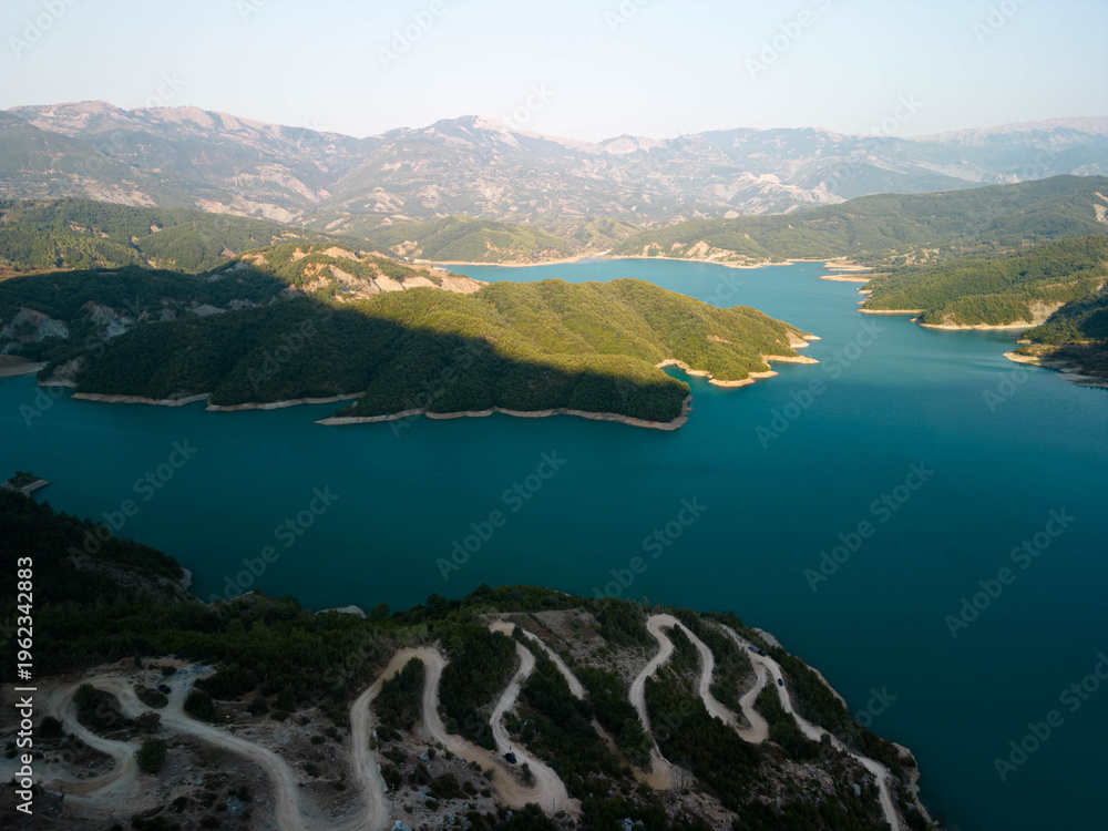 Obraz premium Aerial view of Bovilla Lake with winding mountain road and turquoise water surrounded by green hills near Tirana, Albania in soft sunlight