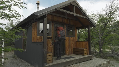 Hiker with a backpack entering a modern wooden mountain shelter in nature