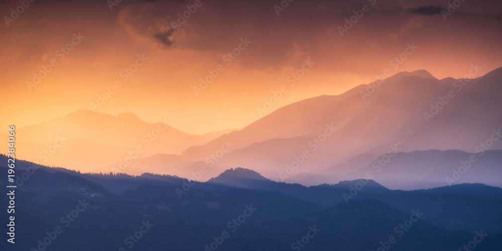 Naklejka premium Silhouettes of Alpine mountains at colorful sunset in summer in Slovenia. Landscape with mountain ridges in fog, golden sunlight and clouds in the evening. Alps. Nature. Hills in sunlight. Scenery