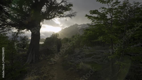 Hiker walking through a forest toward a sunset over the mountains on a stormy day in nature