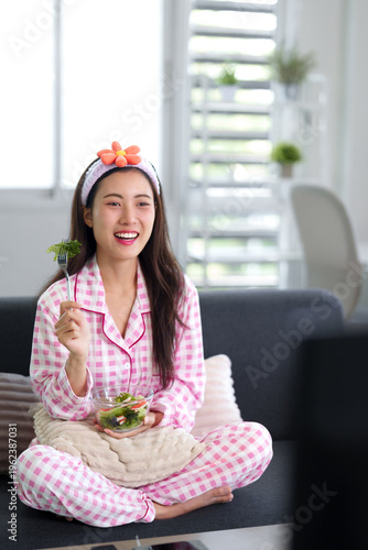 Young Asian woman eating fresh healthy salad enjoying breakfast at home in comfortable pajamas healthy lifestyle wellness