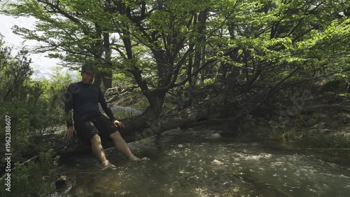 Hiker sitting on a fallen tree over a mountain stream in nature