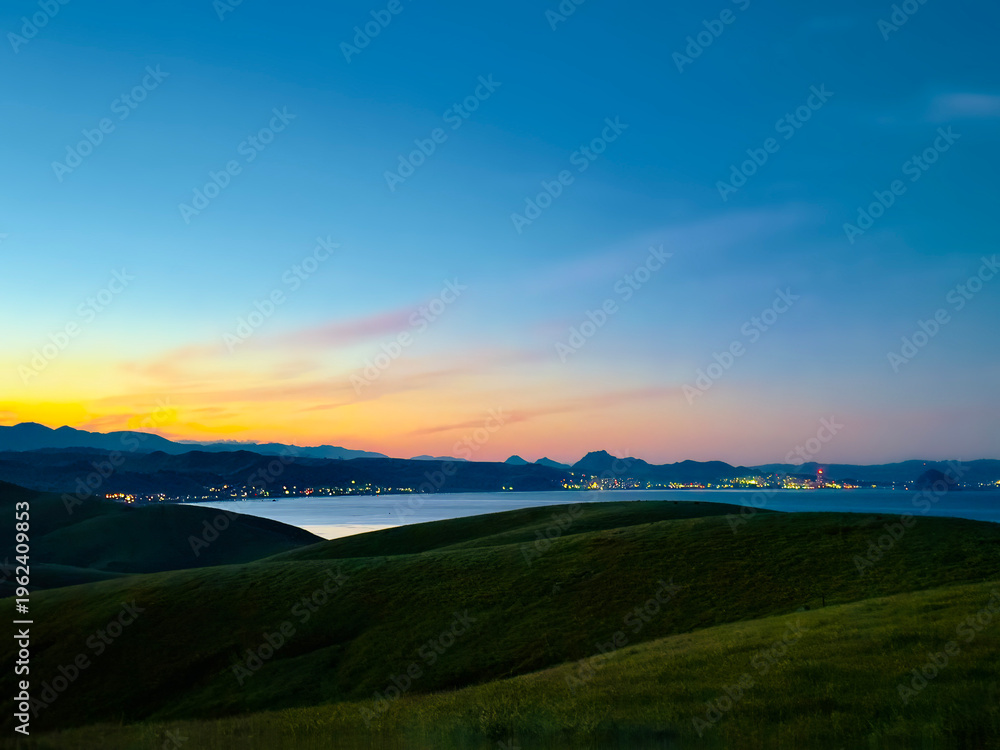 Fototapeta premium View of sunset, sunrise, over hills and ocean and coastline, and city lights