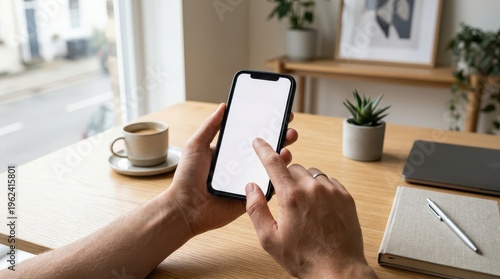 Hands using smartphone with blank screen on desk by window