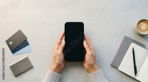 Top view of hands holding smartphone above desk with cards and notebook