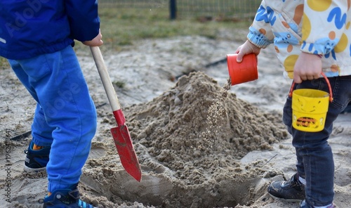 Children boy and girl playing together in sandbox digging sand with shovel and bucket, teamwork and interaction, outdoor playground activity, natural lifestyle moment