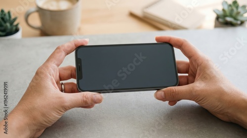 Hands holding smartphone with dark screen in horizontal orientation on tabletop