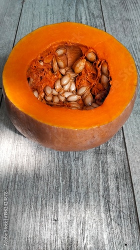 Cut pumpkin with seeds inside on wooden background