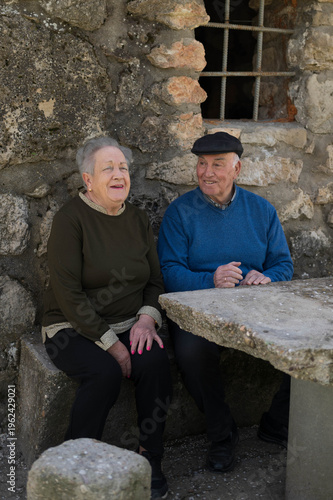 Elderly couple smiling together sitting by stone wall