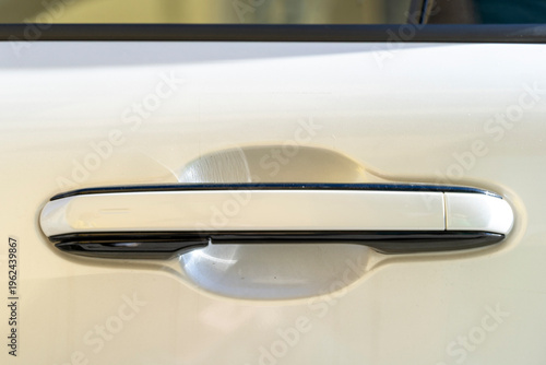 Close-up of a modern vehicle door handle on a white automotive exterior, showing chrome detail