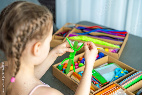 Little girl making craft with colorful materials at table using creative kit at home. Kids creativity development fine motor skills and learning through play concept.
