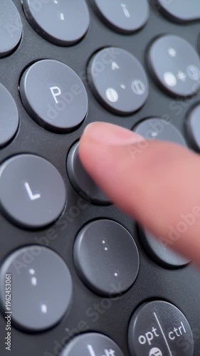 Macro shot of a finger repeatedly pressing the Ñ key on a grey wireless keyboard with circular keys, Concept of Spanish language, digital communication, and typing