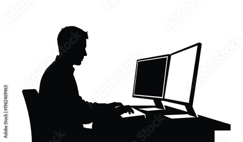 Silhouette of a man sitting at a computer desk working on a desktop pc with a monitor and keyboard in a dark room