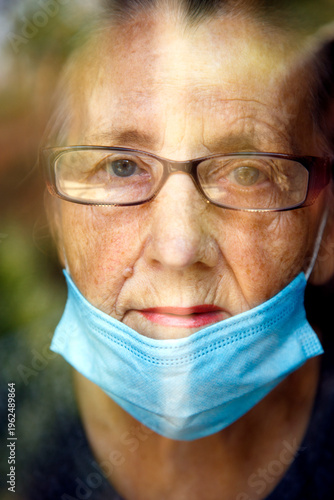 Portrait of an elderly woman in a window after quarantine with her mask removed. An old woman in a window with her mask down, after the pandemic.