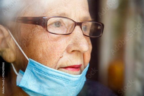 Portrait of an elderly woman in a window after quarantine with her mask removed. An old woman in a window with her mask down, after the pandemic.