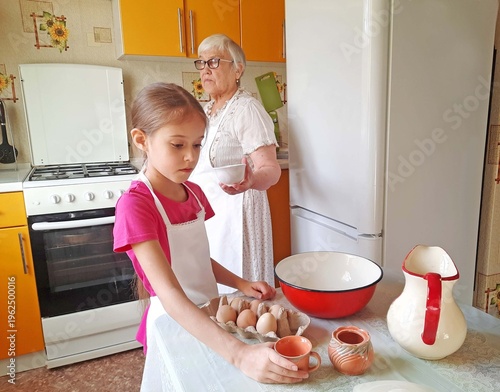 A grandmother and her granddaughter set out the necessary ingredients for cooking on the table.