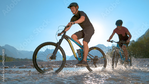 Quadro su tela LOW ANGLE Cheerful young men having fun splashing water while riding their bikes
