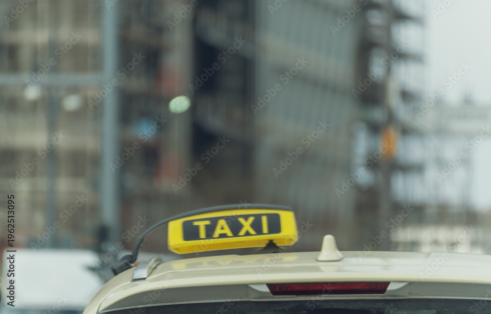 Fototapeta premium Yellow taxi sign atop a vehicle. City background blurred, urban setting. Ideal for transportation, travel, or urban life themes