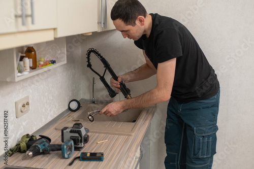 A plumber is replacing a faucet in the kitchen.