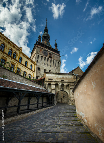 Narrow cobblestone street and clock tower in the background in the old historic town of Sighisoara, Romania.