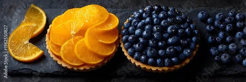 Obraz  z motywem Gourmet Assorted Fruit Tarts Featuring Fresh Orange Slices and Juicy Blueberries on a Rustic Dark Stone Surface, Ideal for Bakery Marketing and Food Photography.