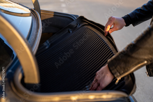Hands placing protective rubber mat into car trunk, closeup of luggage compartment during organization and cargo protection.