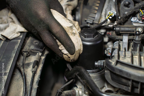Gloved hand cleaning oil filter housing with cloth, closeup of wiping surface during car engine maintenance and service process.