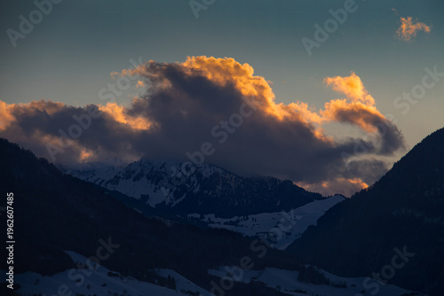 Golden clouds over a snowy mountain; dramatic glowing clouds covering the peak of a dark snowy mountain in Vitznau Switzerland